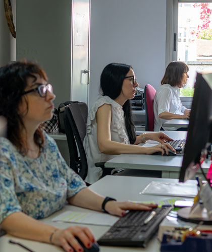 Tres mujeres trabajando frente a ordenadores en una oficina, en fila junto a una ventana